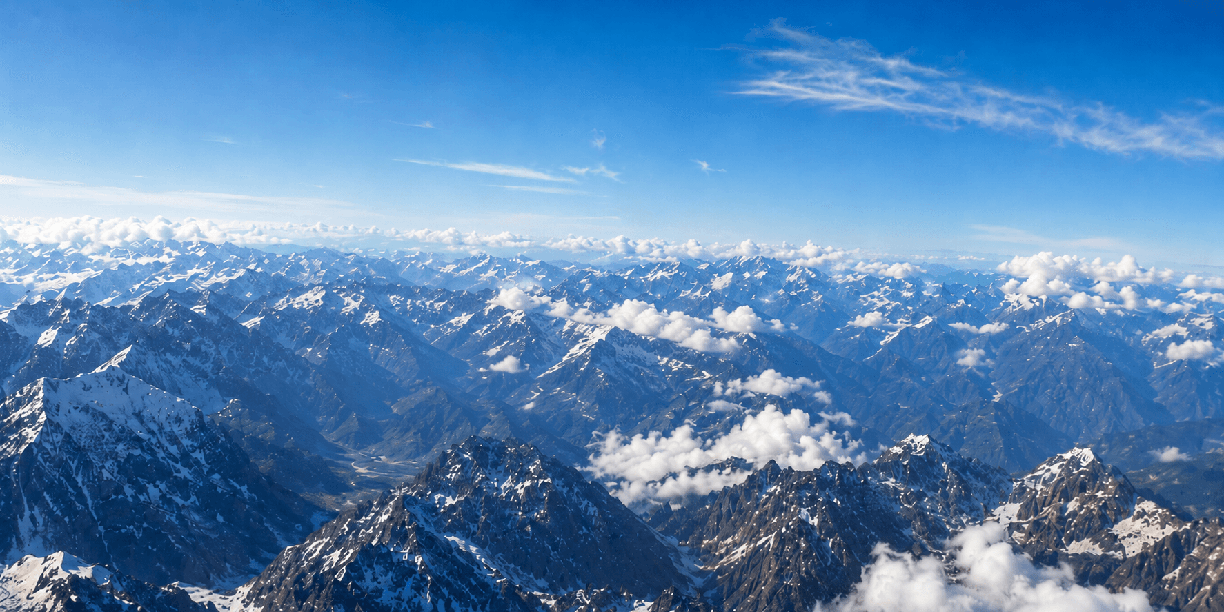 Snow-capped mountain peaks under a blue sky, seen from above